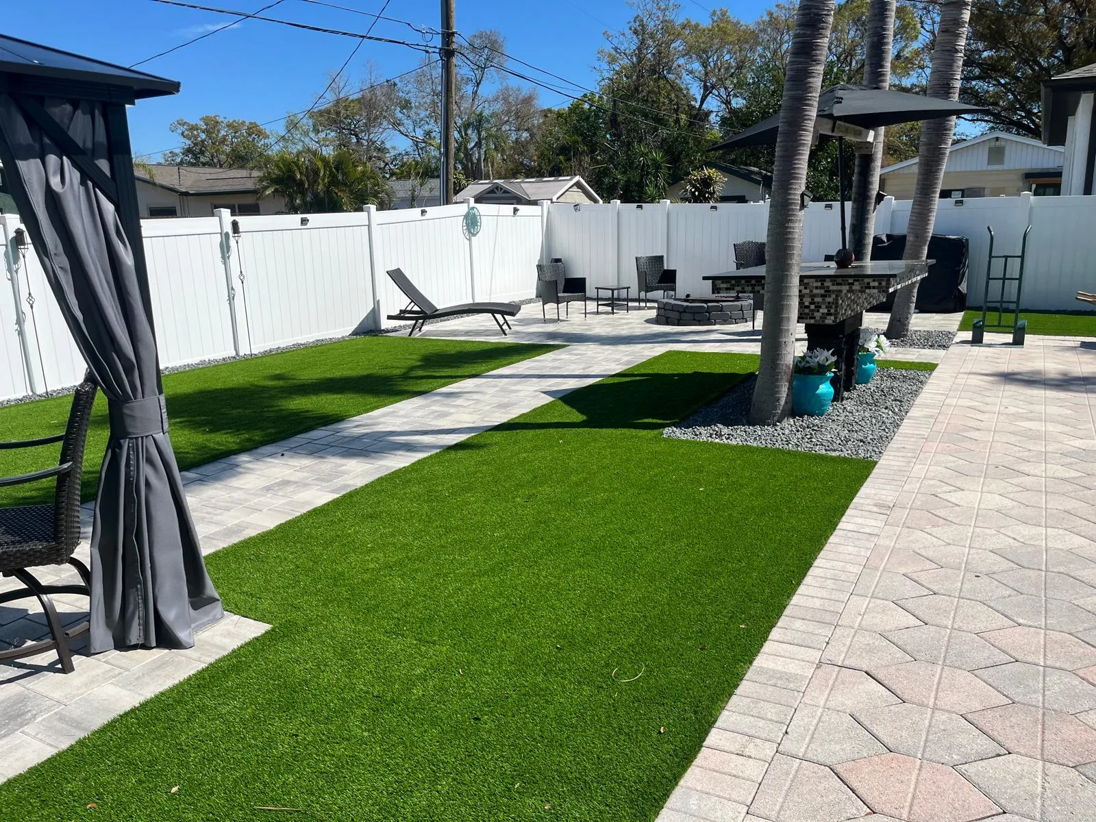 Curved gray paver path with artificial turf in a backyard
